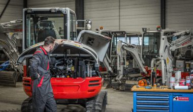 Takeuchi monteur bij graafmachine met motorkap open