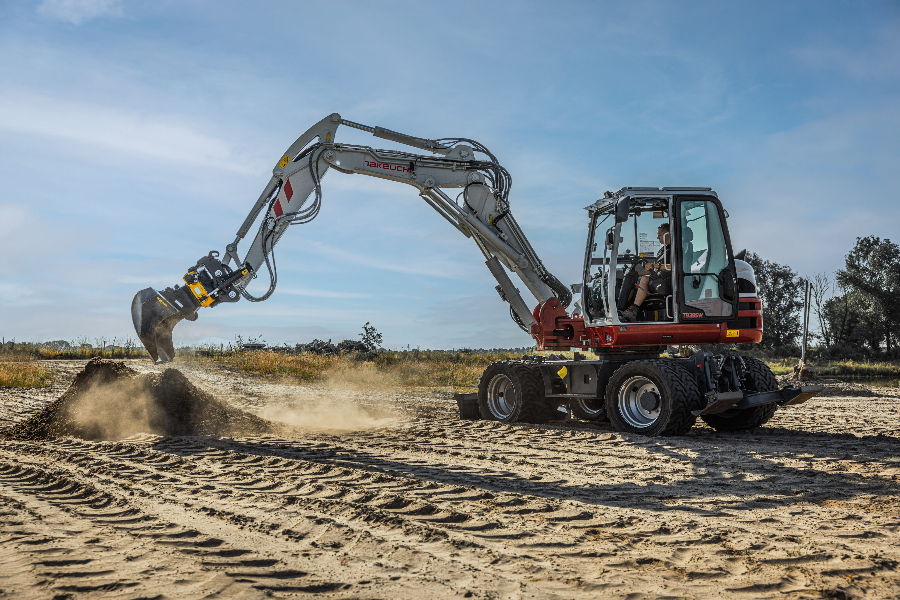 De Takeuchi tb395w graafmachine die zand lost op de grond met de graafbak