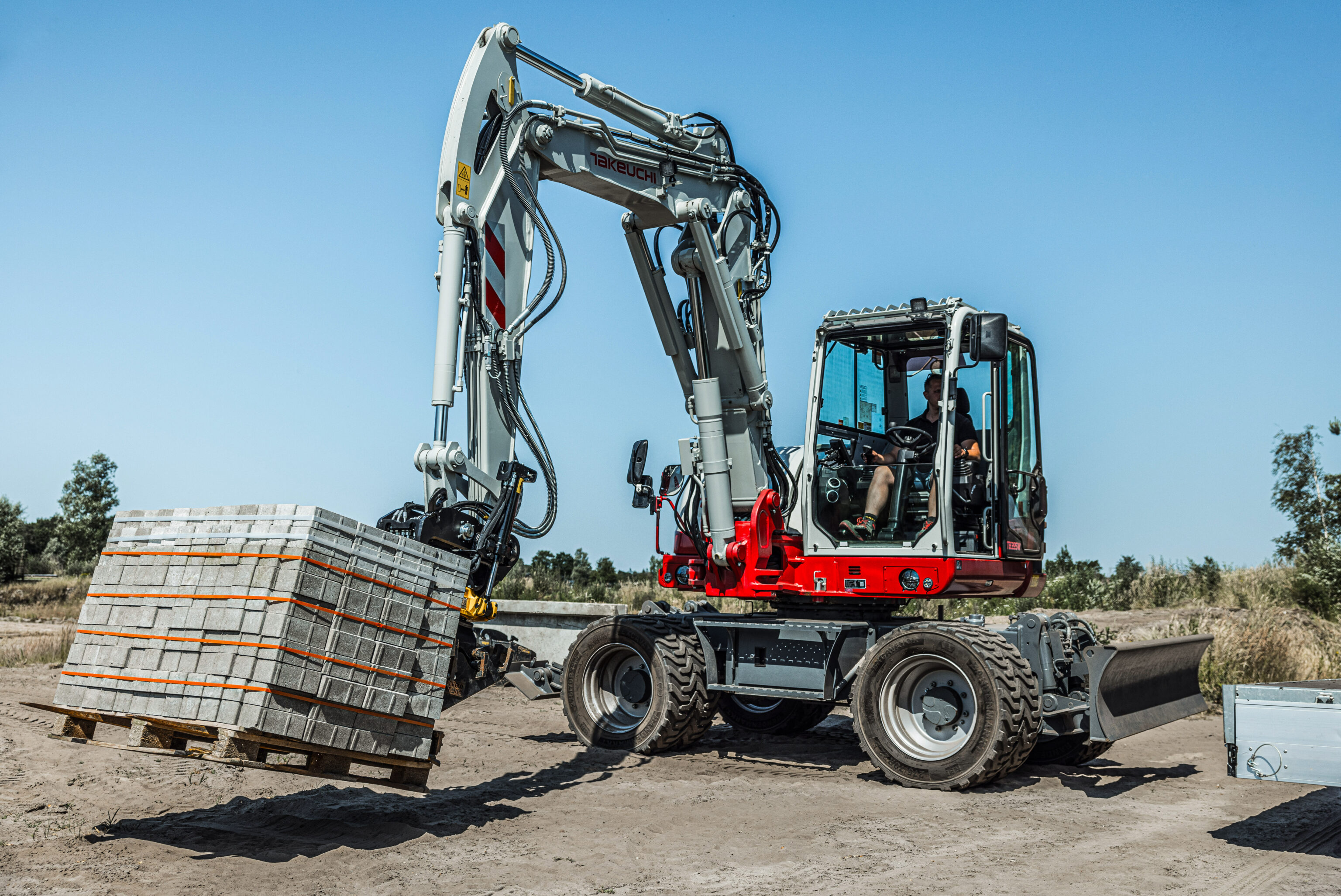 tb395w-graafmachine van takeuchi die met een pallettanden aanbouwstuk een pallet klinker verplaatst