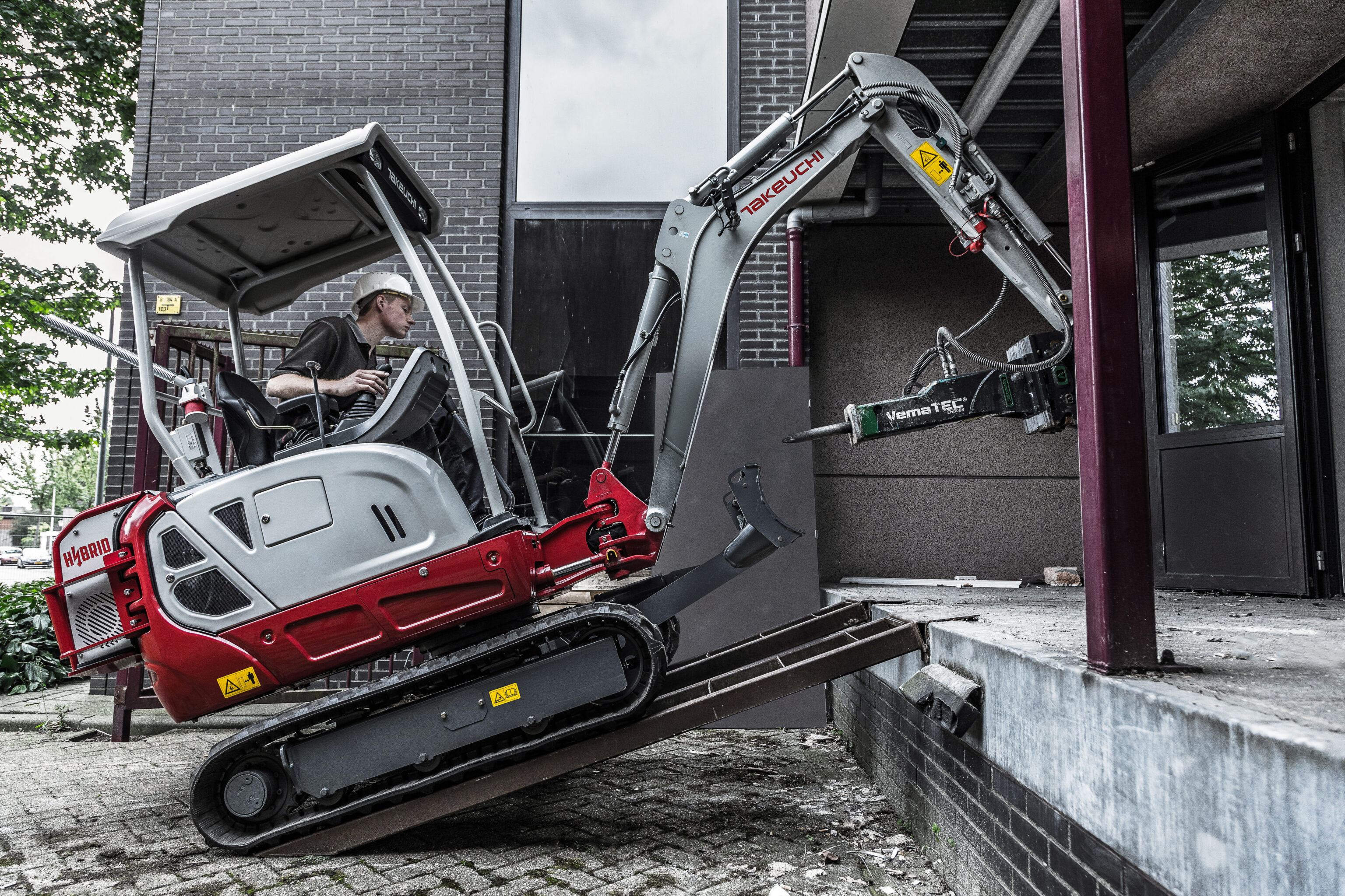 emissievrije hybride takeuchi rijdt via oprijplaten een pand binnen met een hydraulische sloophamer