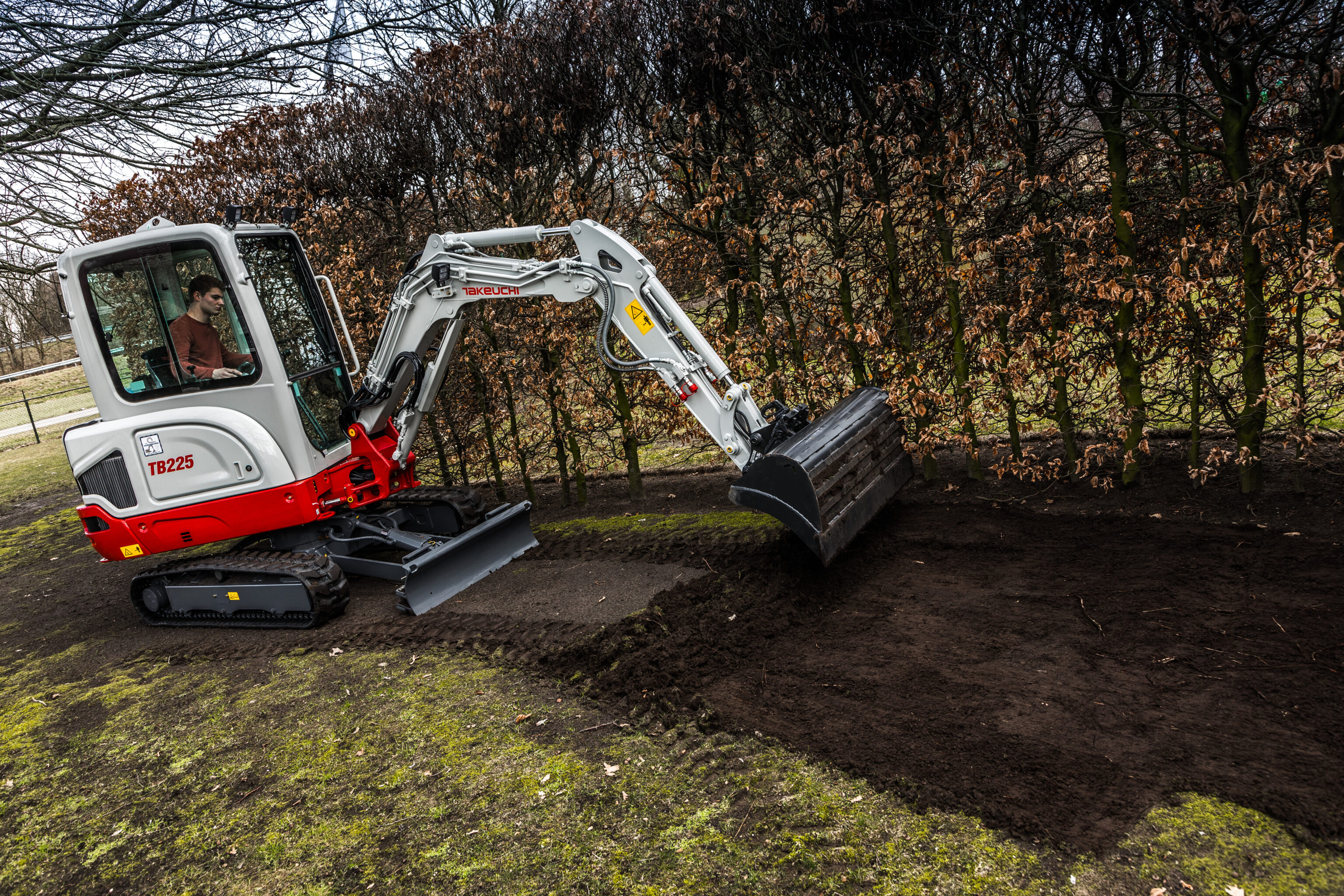 Takeuchi graafmachine die een tuin met een slotenbak aan het nivelleren is