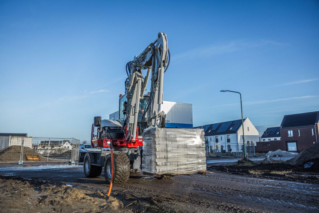 Takeuchi graafmachine verplaatst een pallet klinkers in een nieuwbouwwijk